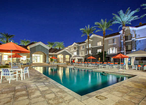 Dog-Friendly Townhomes in Phoenix, AZ - The Highland Apartments - Resort-Style Pool At Night With Palm Trees, Lounge Chairs, Umbrellas, and Apartment Buildings Surrounding The Courtyard.
