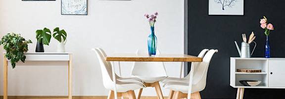A dining room with a white table and chairs, a black and white rug, and framed pictures on the wall.