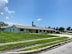 A blue building with a white roof is surrounded by a grassy area and a paved road.
