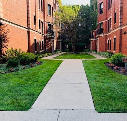 A walkway leads through a green lawn between two red brick buildings.