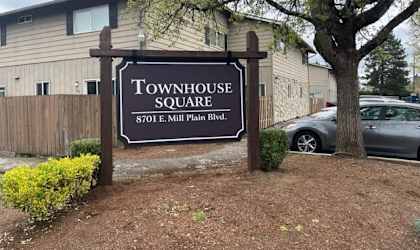 A sign for Townhouse Square is in front of a tree and a car.