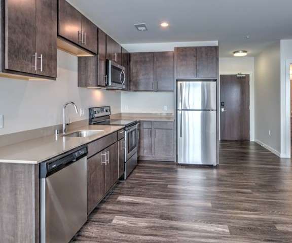 A large, modern kitchen with stainless steel appliances, kitchen utensils, marble countertops with lots of room, and large, gray wooden cabinets at Stitchweld Apartment Homes. 