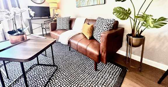 A living room with a brown leather couch, a coffee table, and a potted plant.