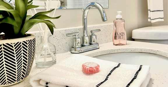 A bathroom sink with a potted plant, soap, and a towel.