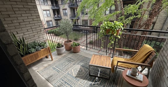 A balcony with a table, chairs, and potted plants.
