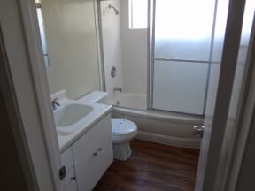 Bathroom with white cabinets and fixtures, hardwood flooring, and natural light at Villa Knolls Apartments in La Mesa, California.