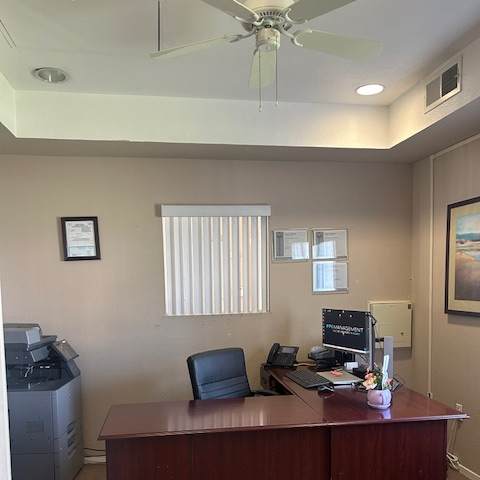 A room with a ceiling fan, a window with blinds, and a cabinet with a monitor on top.