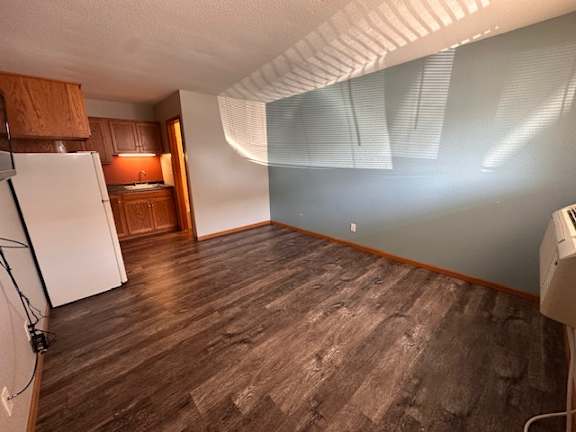 A room with a white refrigerator and wooden flooring.