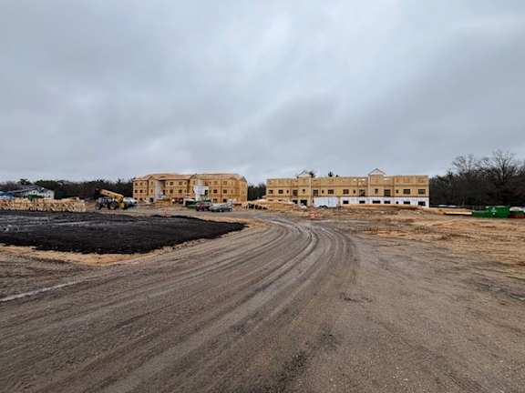 A construction site with a large building under construction and a dirt road leading to it.
