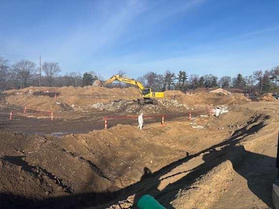 A construction site with a yellow excavator and orange cones.