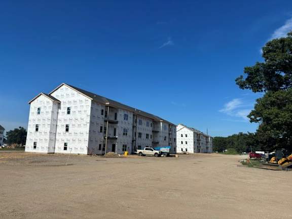 A large white building with many windows is surrounded by a dirt lot.