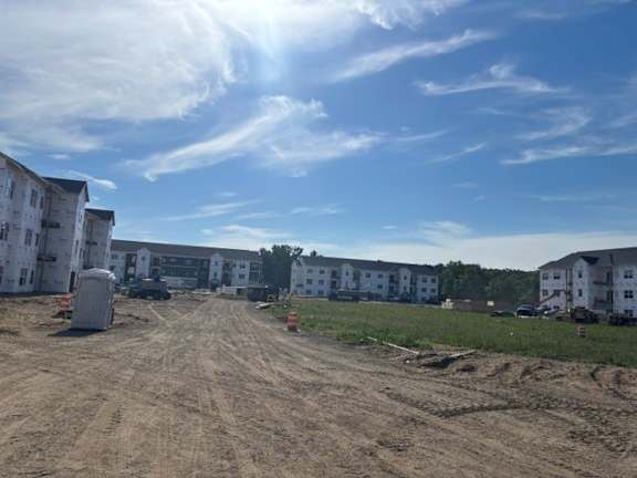 A construction site with a dirt road and white buildings in the background.