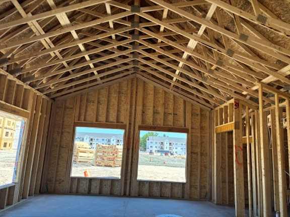 A room under construction with wooden beams on the ceiling and windows showing the exterior.