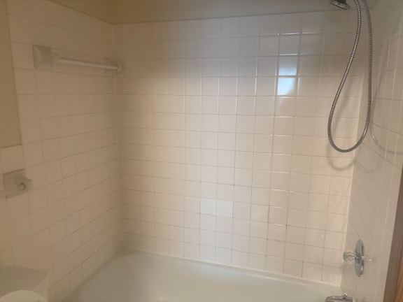 A white tiled bathroom with a white tub and a white shower head.