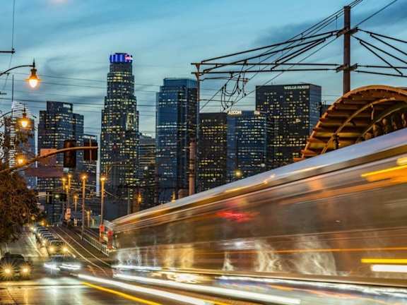 A long exposure shot of a city street at night with a moving train in the foreground.