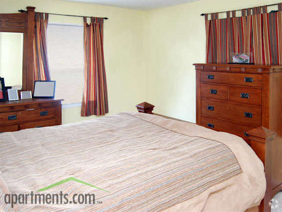 large carpeted bedroom with cedar dresser and windows with drapes