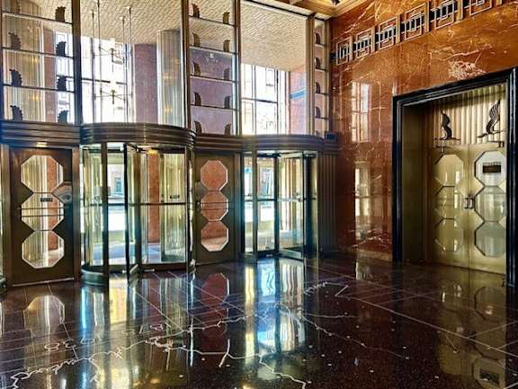 A hallway with marble floors and a series of doors with windows.