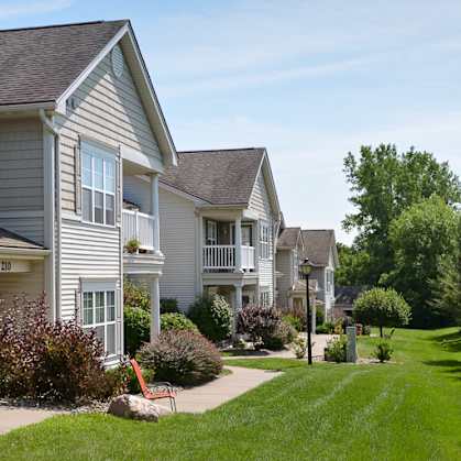 Exterior view of apartment buildings with sidewalks, lawn, lighting, and trees/landscaping
