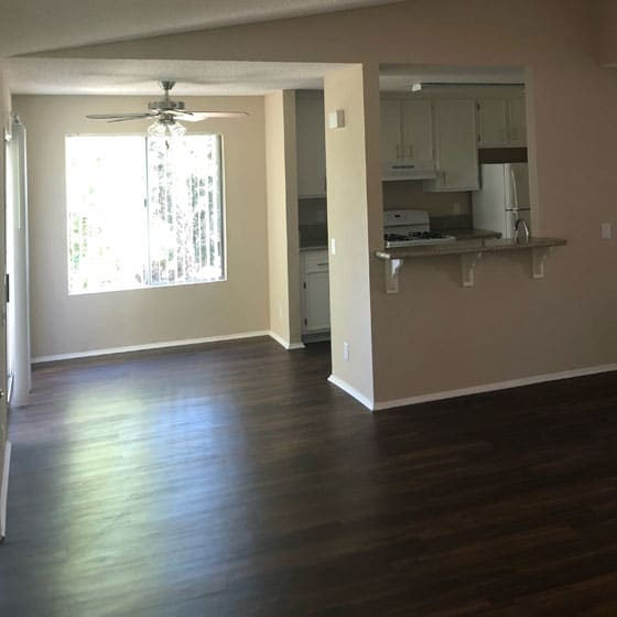 an empty living room with a kitchen in the background