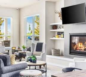 A living room with a grey couch, a coffee table, a fireplace, and a flat screen TV mounted on the wall.