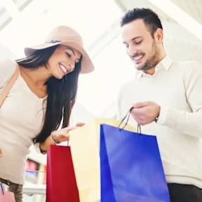 A man and a woman are shopping together, holding colorful bags.