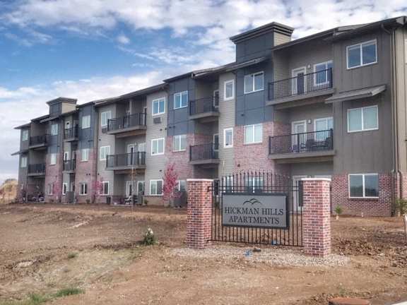 A multi-story residential building with a sign that reads "Hickman Hills Apartments.".