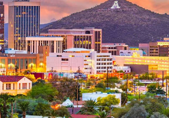 A cityscape with a mountain in the background and buildings illuminated at dusk.