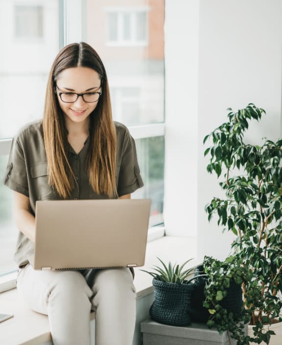 a woman sitting on a window sill using a laptop computer