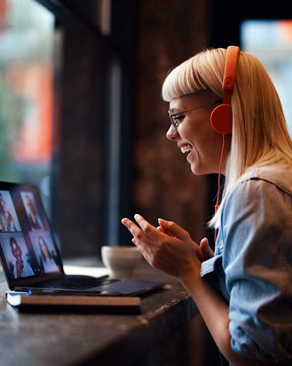 A woman with headphones is talking on the phone while looking at her laptop.