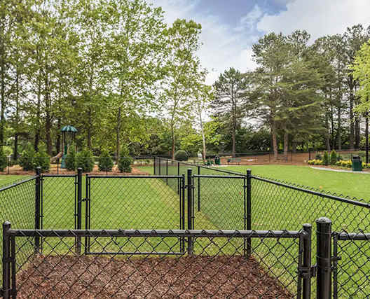 A baseball field surrounded by a black fence with trees in the background.