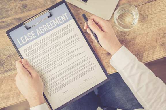 A person is signing a lease agreement on a clipboard.