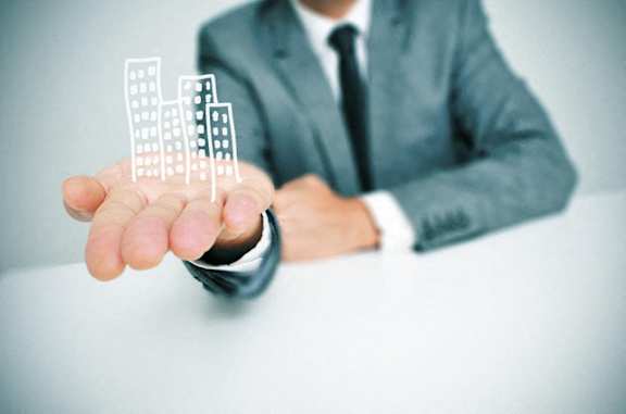 A man in a suit is holding a 3D model of buildings in his hand.