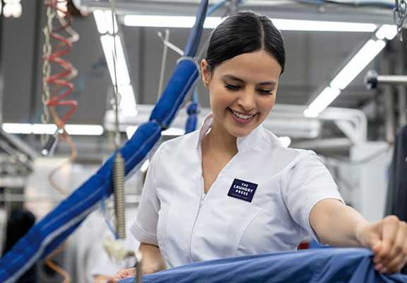 A woman in a white shirt is working on a blue shirt in a factory.