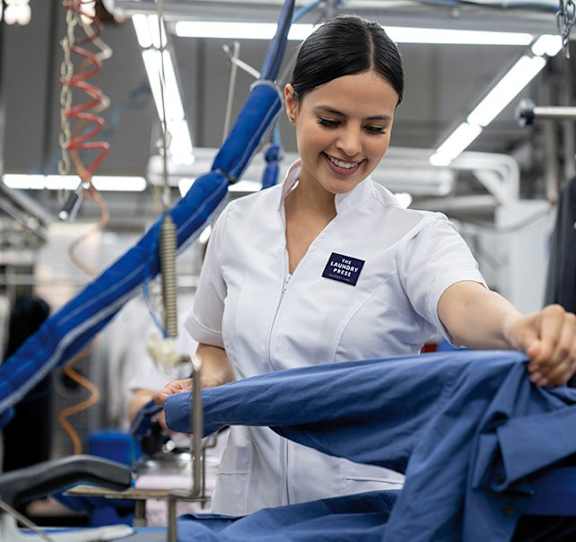 A woman in a white shirt is working on a blue shirt in a factory.
