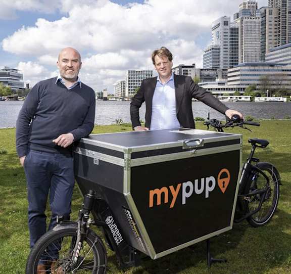 Two men standing next to a mypup cart with a bicycle.