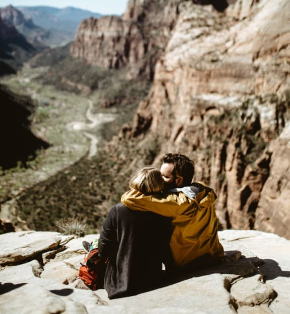 a couple of people sitting on a rock overlooking a canyon