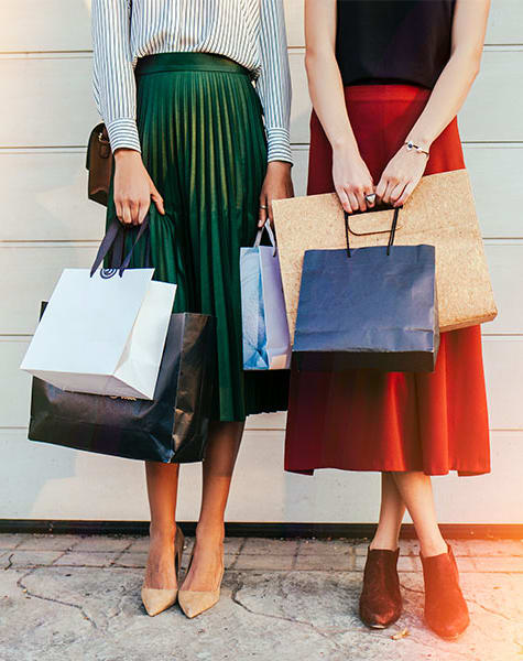 two women holding shopping bags and standing next to a white wall
