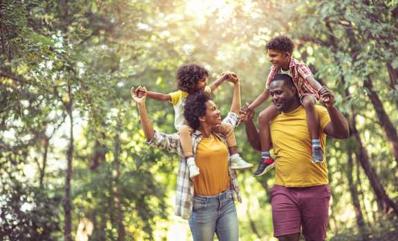 a family walking through the woods with a child on their shoulders