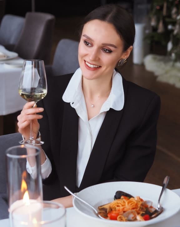a woman in a business suit sitting at a table in a restaurant with a glass of wine