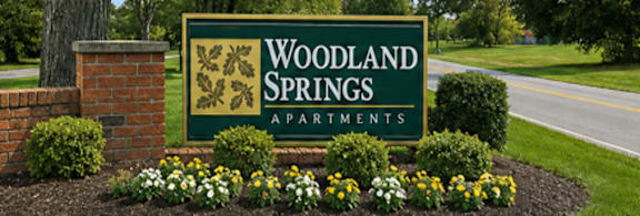 A sign for Woodland Springs Apartments is surrounded by flowers.