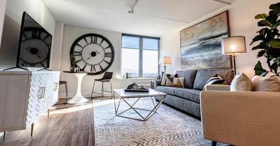 A living room with a grey couch, a coffee table, and a large clock on the wall at Cityplace Apartment Homes Apartments, Allentown, PA, 18101