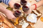 people raising glasses of red wine over a wooden table with cheese and olives