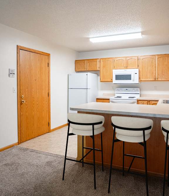 A room with a carpeted floor and a window with blinds. Fargo, ND Crown Court 2 Apartments
