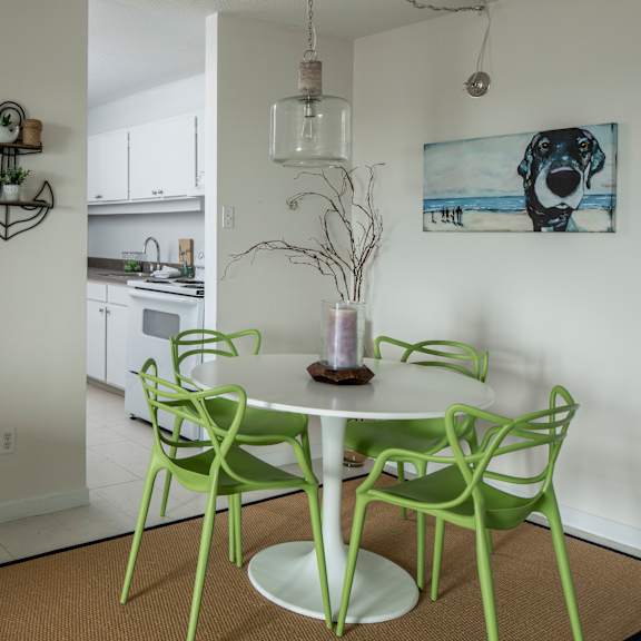 A white dining table with green chairs and a vase of dried branches on it.