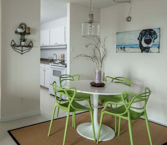 A white dining table with green chairs and a vase of dried branches on it.