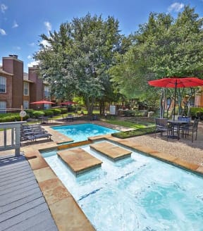 Pool and sundeck with trees and an umbrella at Cobblestone Apartments in Arlington, Texas