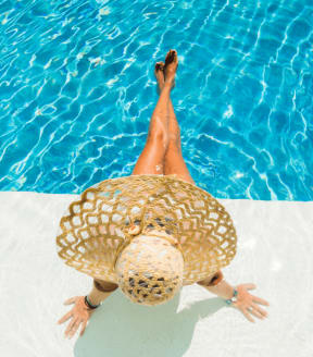 Woman with a straw sunhat sitting with her legs in the pool at Cobblestone Apartments in Arlington, TX