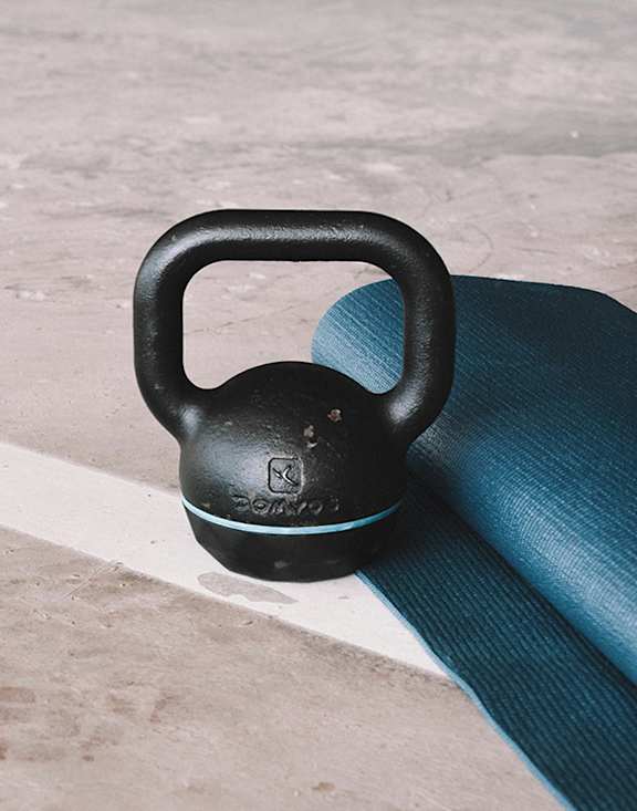A black kettlebell rests on a blue yoga mat.