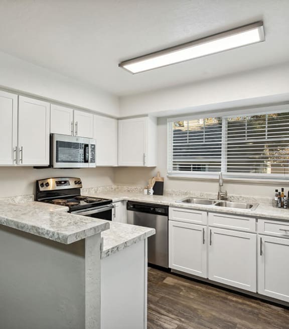 Model Kitchen with White Cabinets and Wood-Style Flooring at Broadmoor Village Apartments located in West Jordan, UT-SMLAM.
