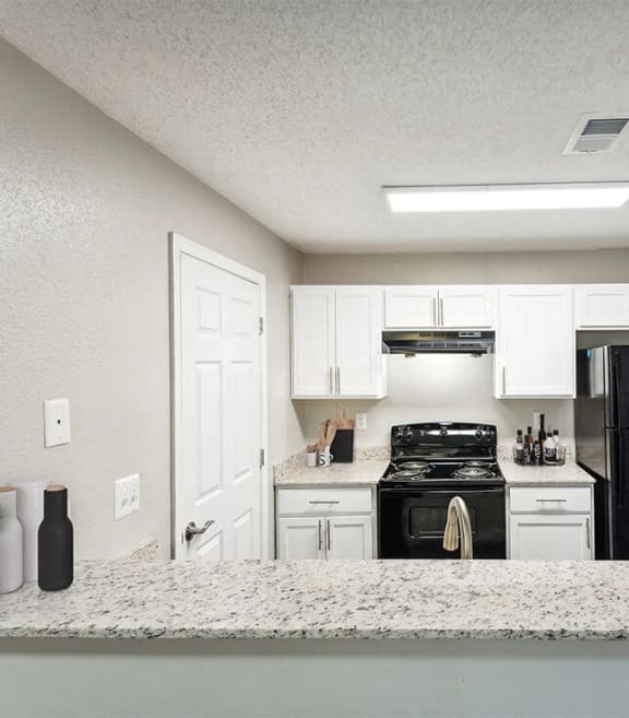 Model apartment kitchen with white cabinets and a black stove and refrigerator